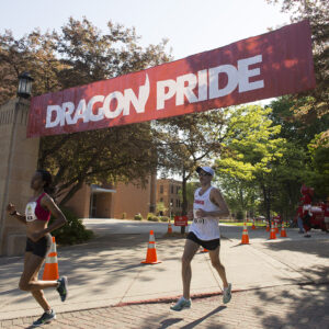 Fargo Marathon runners pass under Dragon Pride sign as they run through MSUM campus.