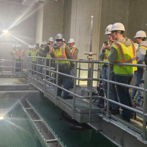 A group of Construction Management students tour an indoor construction site. The group is examining a large water basin.