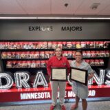 Drs. Ellen Fagerstrom and Julia Poplin hold plaques in front of an illuminated Dragons sign