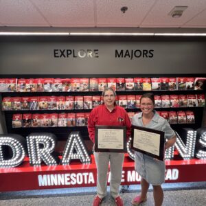 Drs. Ellen Fagerstrom and Julia Poplin hold plaques in front of an illuminated Dragons sign